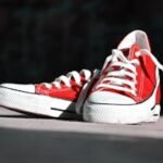 Close-up of vibrant red canvas sneakers with white laces on an outdoor surface.